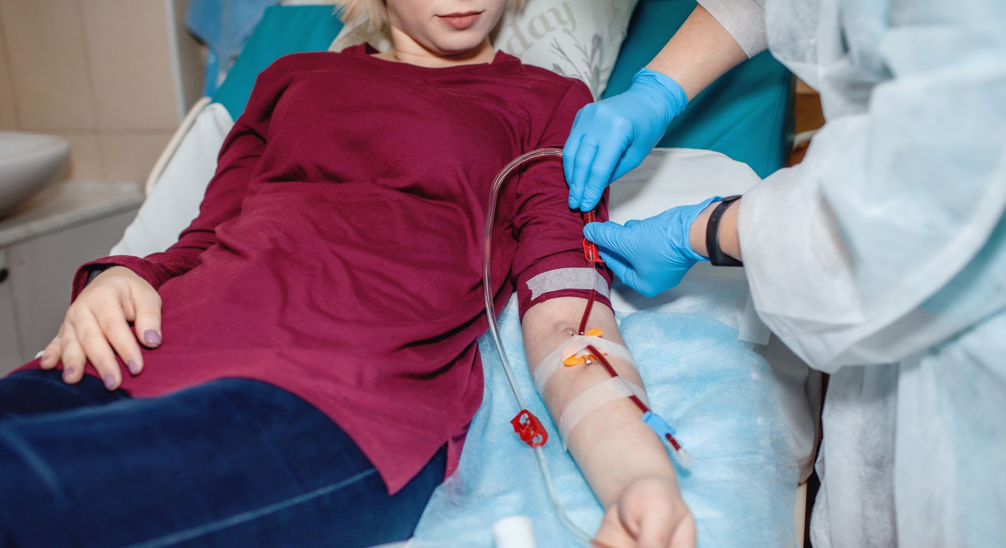 A medical worker in gloves attends to a person lying on a hospital bed with an intravenous line, possibly receiving treatment such as EBOO ozone therapy, as patients often inquire about the EBOO ozone therapy price before procedures.